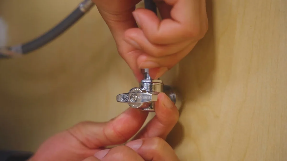 Plumber turning an under-sink shutoff valve before a faucet repair