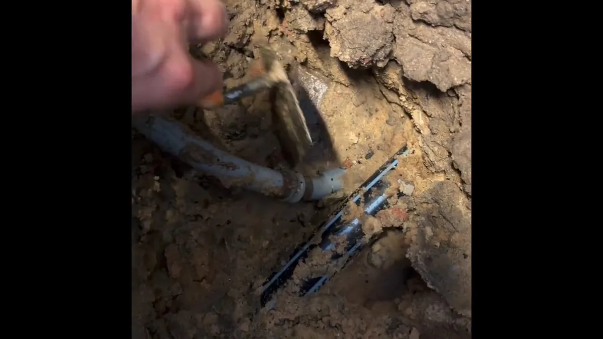Plumber repairing an exposed sewer line section during excavation